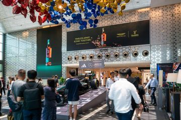 Two JCDecaux digital screens over the entrance to Raffles City, running a whisky campaign above a Formula One car on display, with shoppers walking past.
