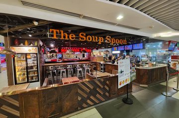 A The Soup Spoon outlet, its name in orange letters above high tables and stools, with the ordering counter and menu screens behind.