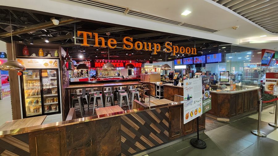 A The Soup Spoon outlet, its name in orange letters above high tables and stools, with the ordering counter and menu screens behind.