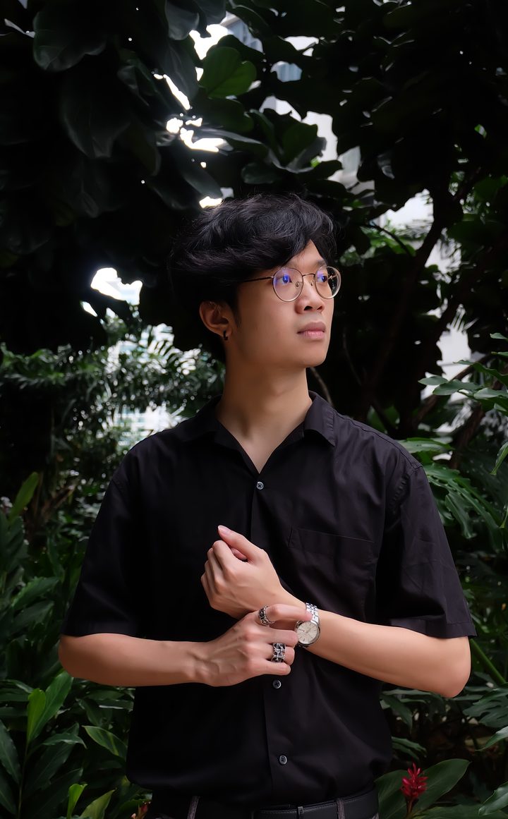 Tham Yu Le, standing among foliage in a black shirt.